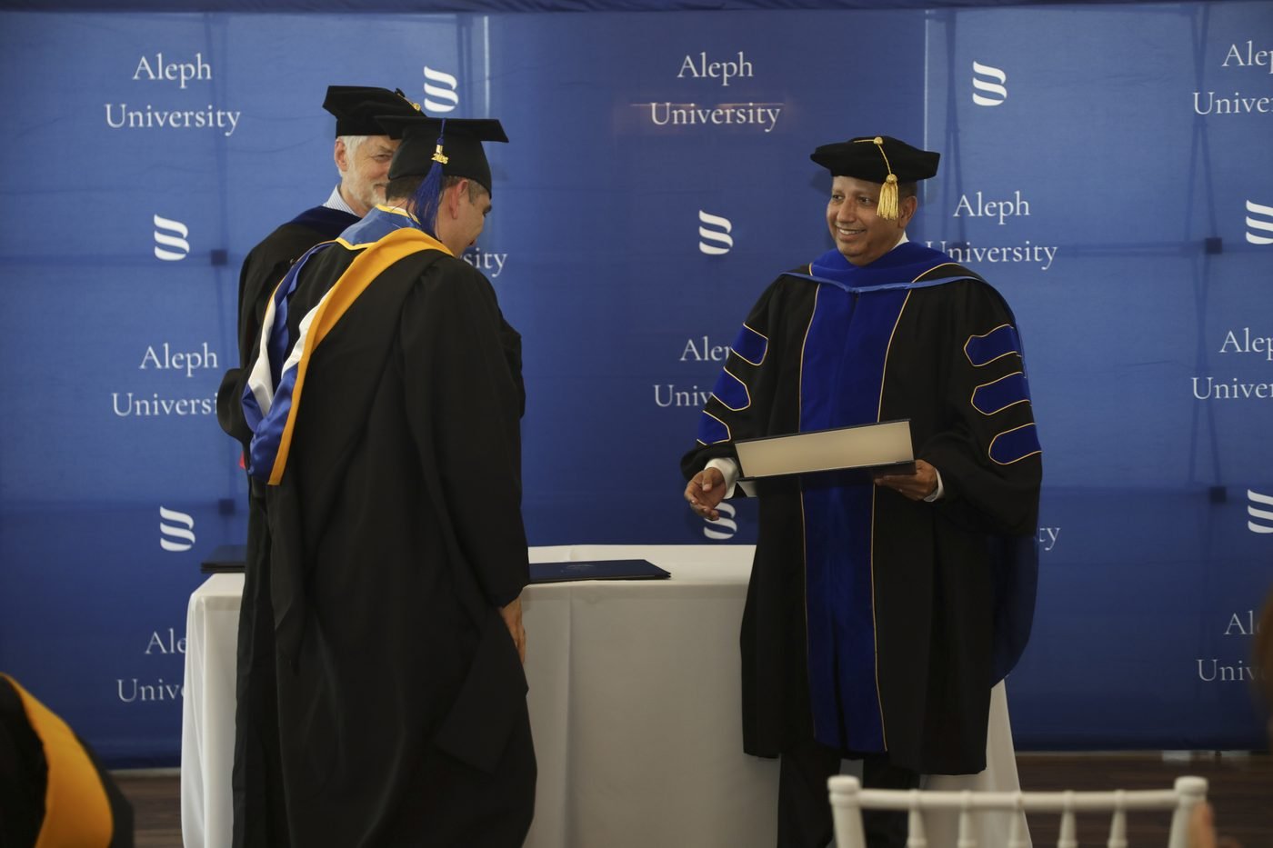 Un graduado cruzando el escenario para recibir su diploma frente al telón de fondo de Aleph University.