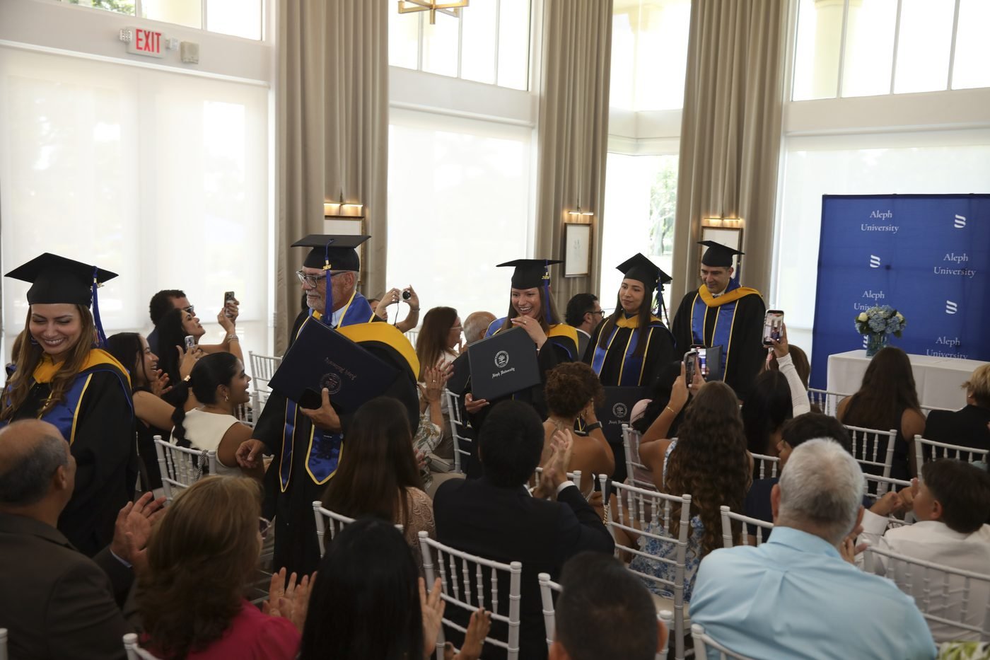 Graduandos avanzando por el salón mientras las familias y los invitados aplauden durante la ceremonia de graduación 2026 de Aleph University.